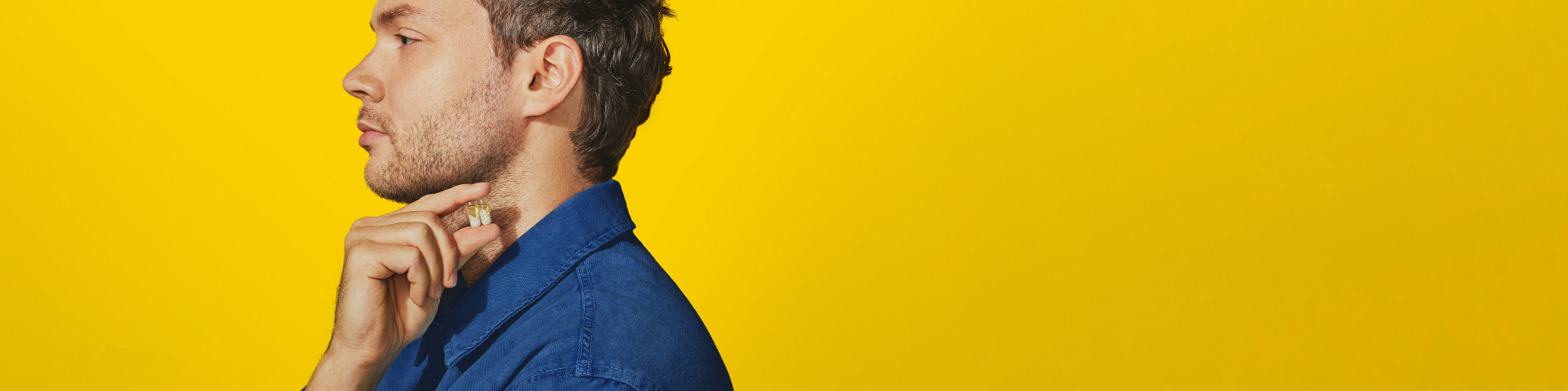 A man in a blue shirt holding two multivitamins against a yellow background.