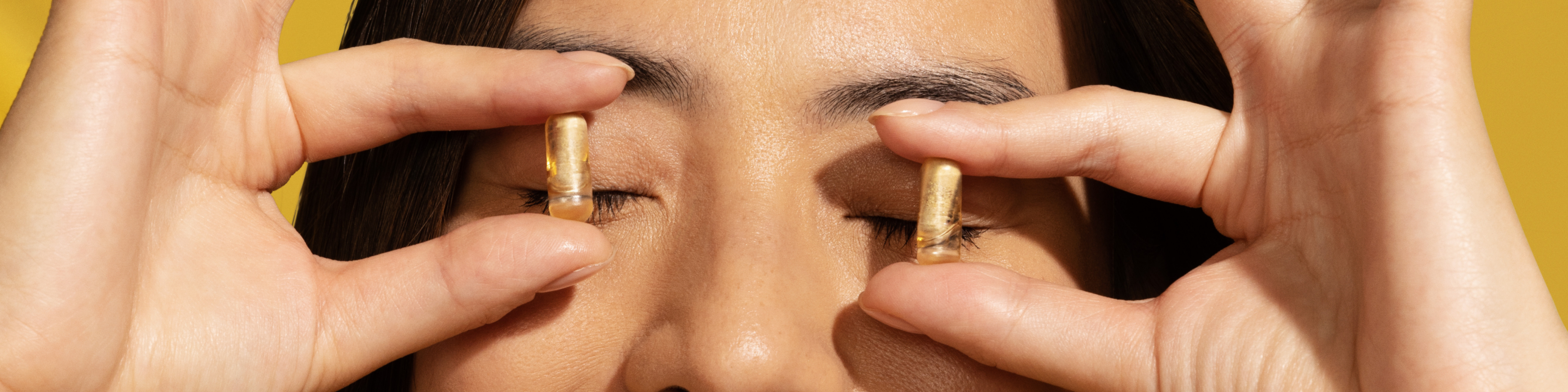 Woman holding two prenatal multivitamins over her eyes.